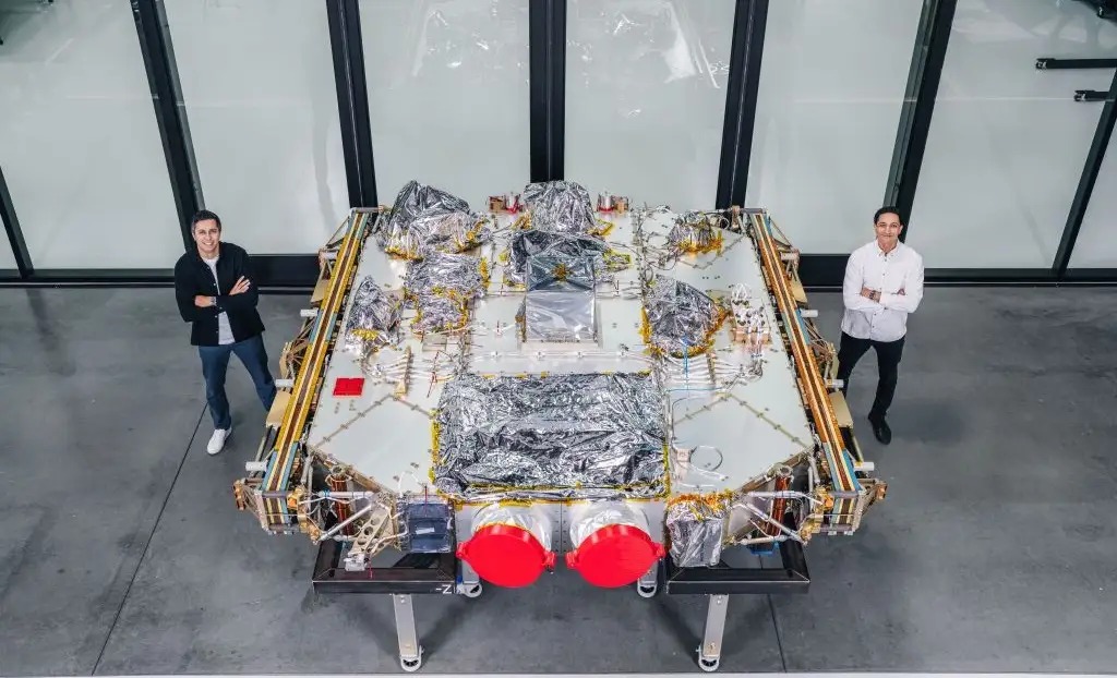 Karan and Neel Kunjur standing beside a large K2 Space satellite in a factory