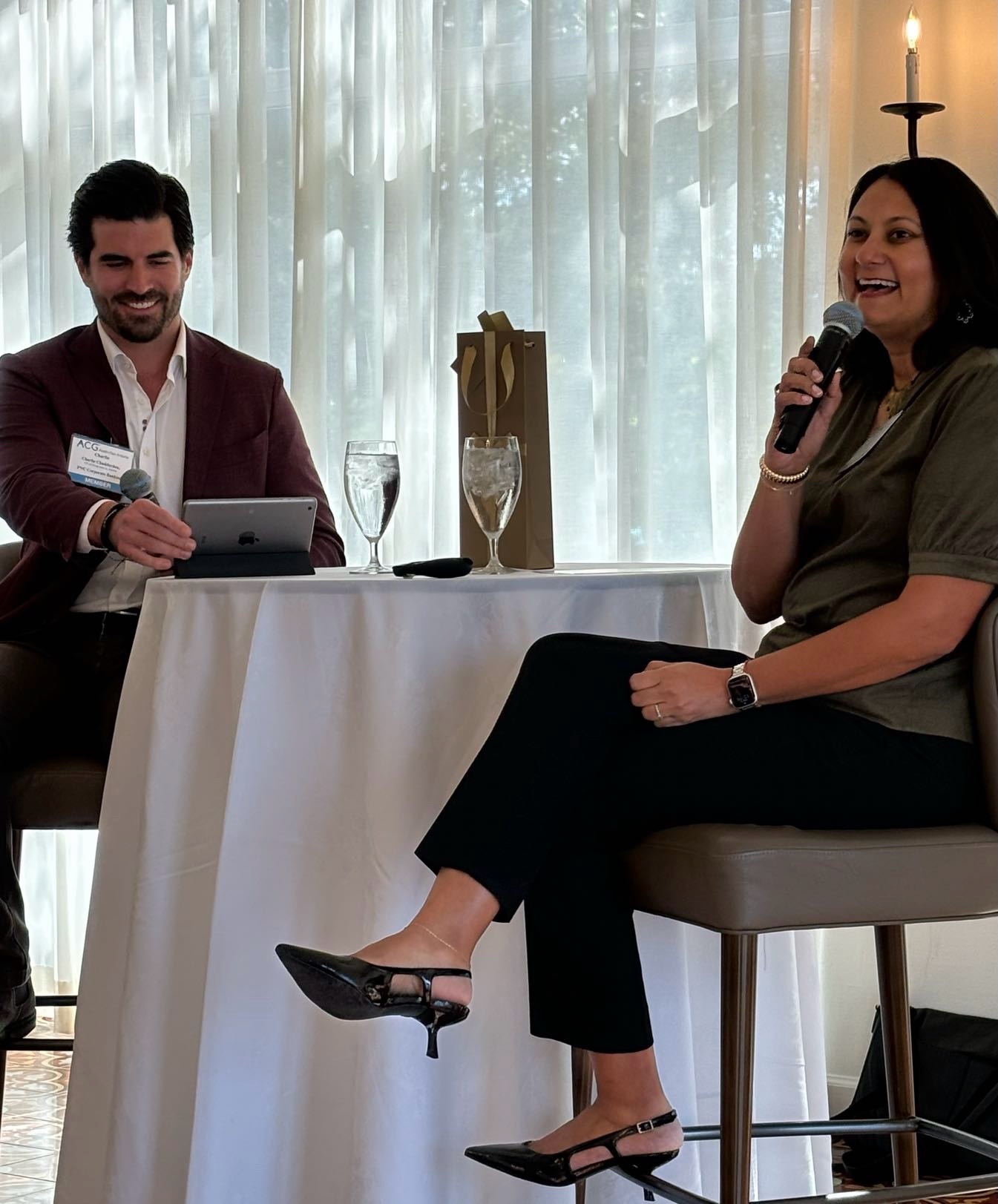 Neha Sampat speaking into a microphone during an Association for Corporate Growth lunch