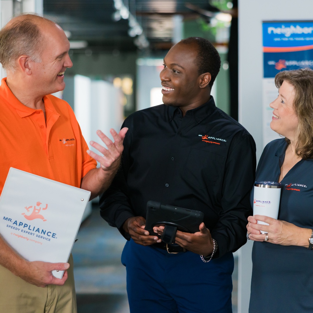 Three Mr. Appliance franchise owners talking, with a folder, tablet and branded tumbler