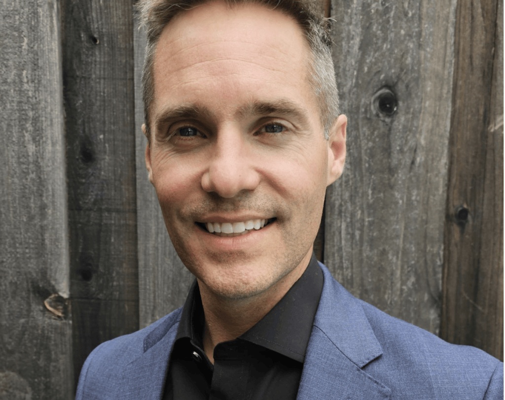 Neil Daly in a blue jacket, photographed in front of a timber fence