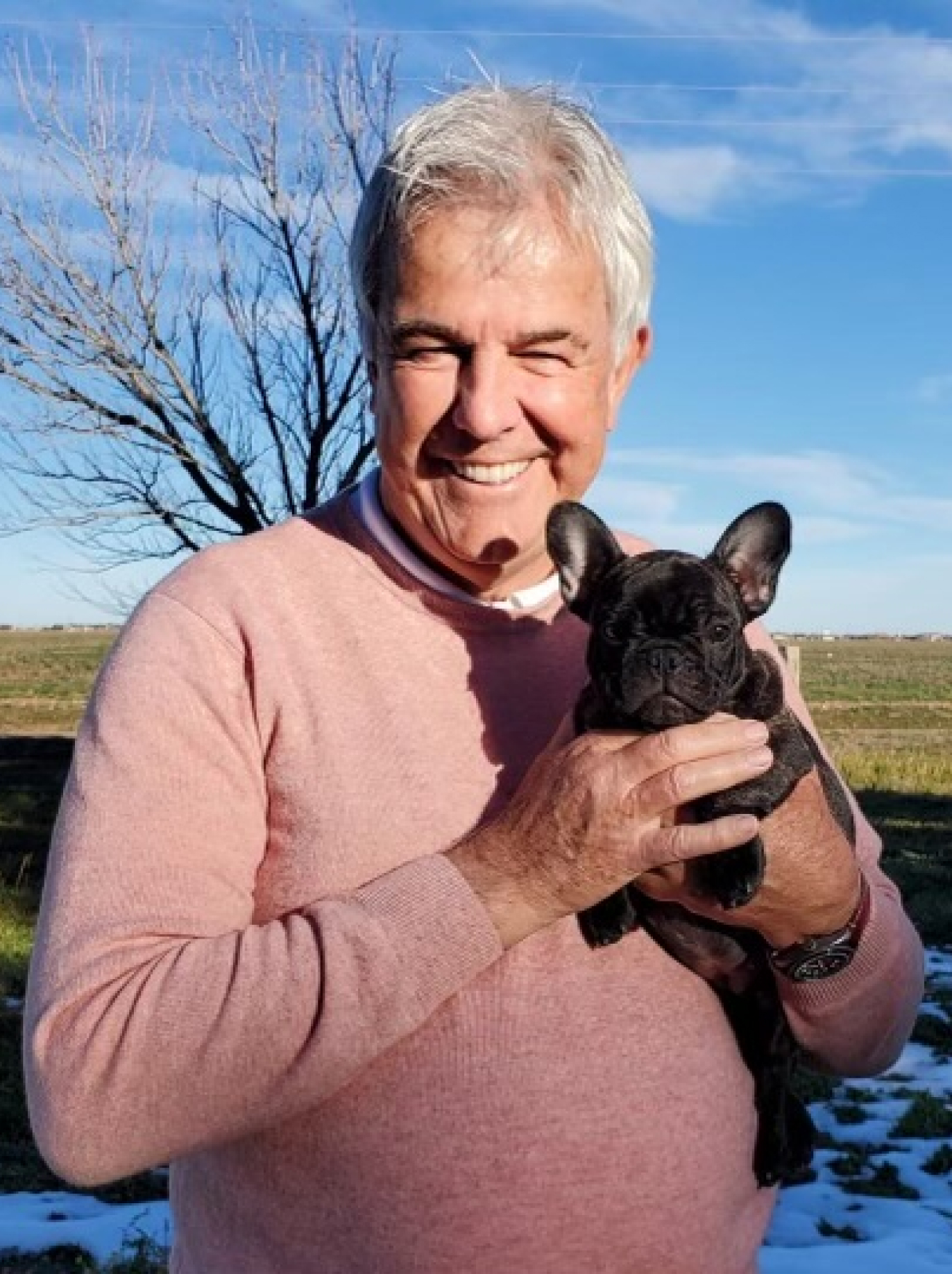 Neil Matheson outdoors, smiling while holding a small black dog