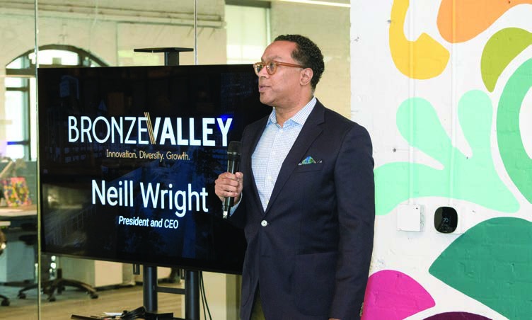 Neill S. Wright holding a microphone beside a screen bearing his name and Bronze Valley’s name