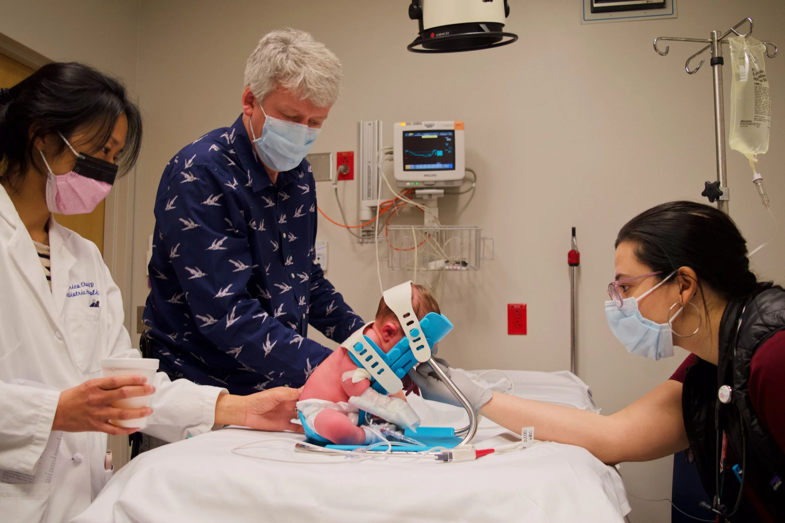 Clinicians using a blue and white SMöLTAP infant-positioning device in a hospital room