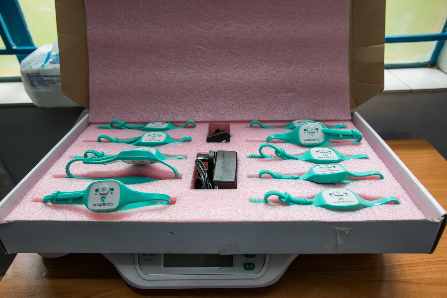A case of teal neoGuard wearable monitors arranged around a charging adapter