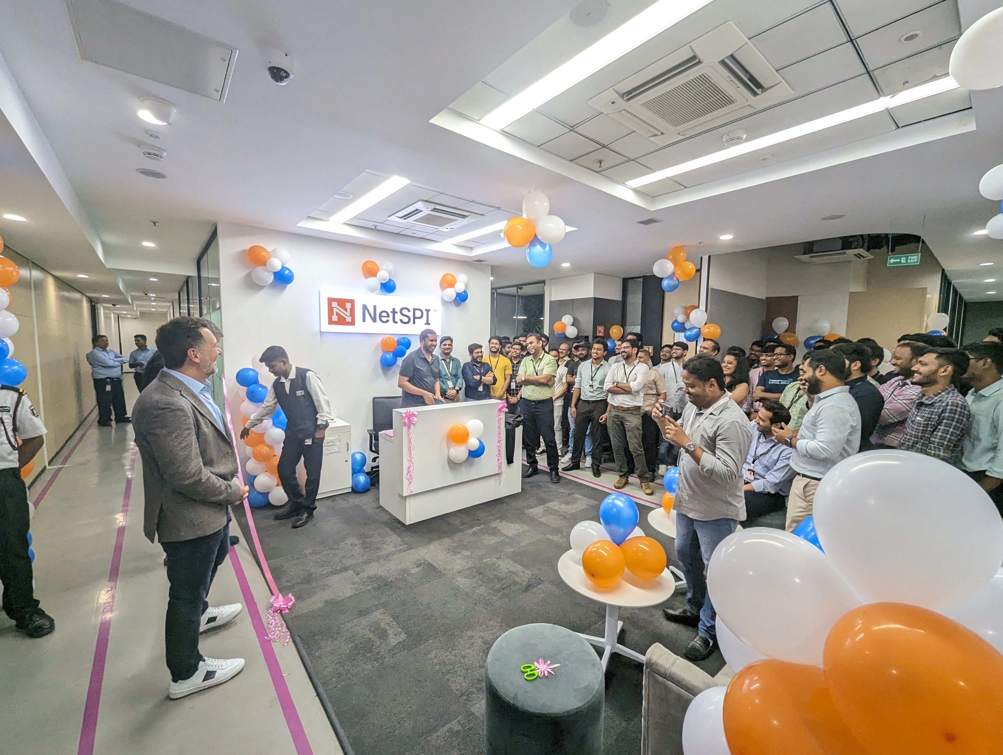 NetSPI colleagues gather around a ribbon in a decorated Pune office