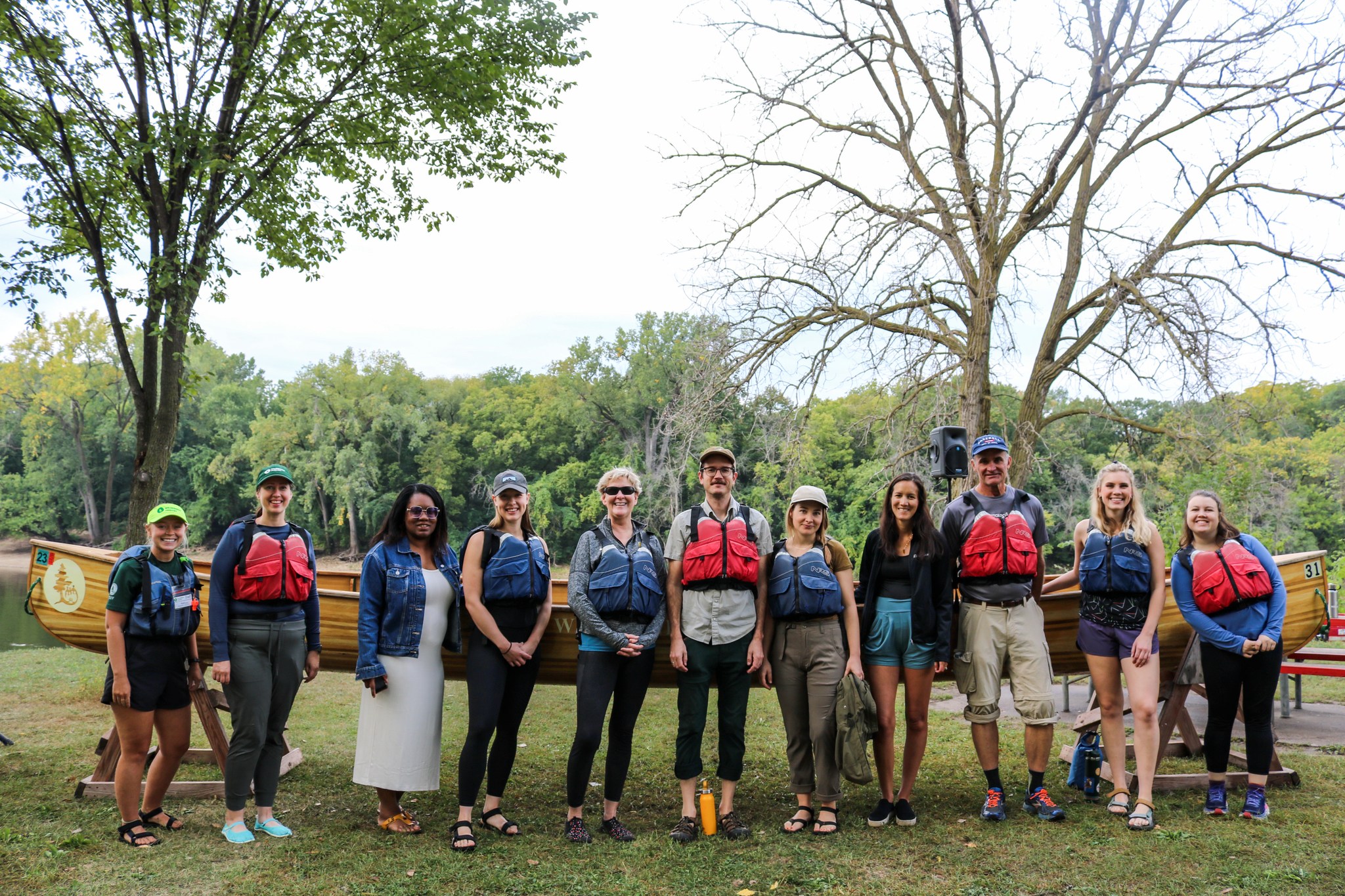 Members of the Neuger team gathered outdoors in front of canoes