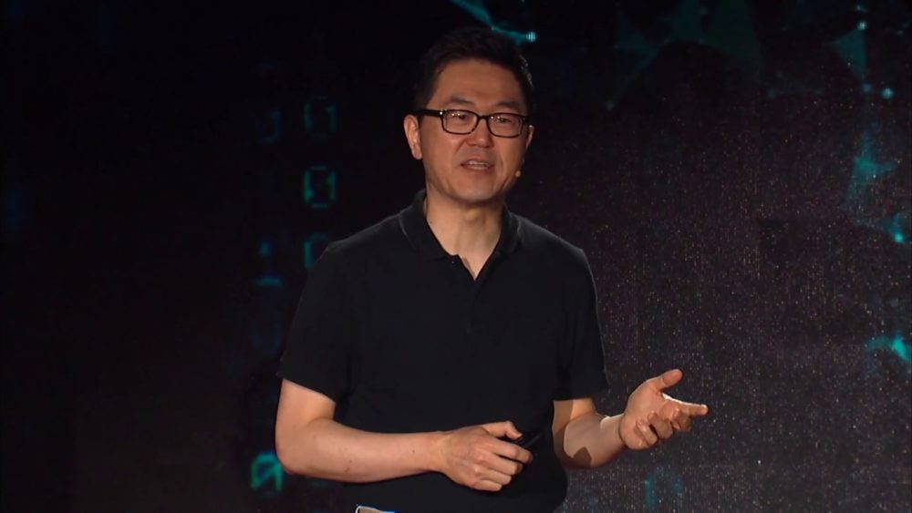 Daeyeol Lee mid-talk in front of a dark, data-patterned stage