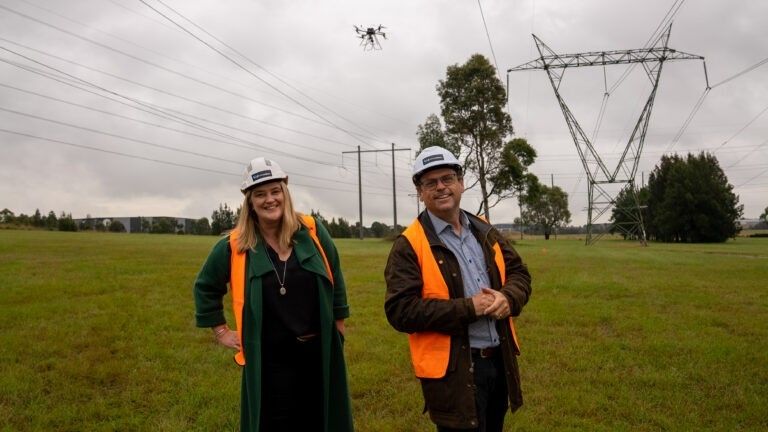 EnergyLab CEO Megan Fisher and then-New Energy Nexus CEO Danny Kennedy wearing safety vests beneath electricity pylons