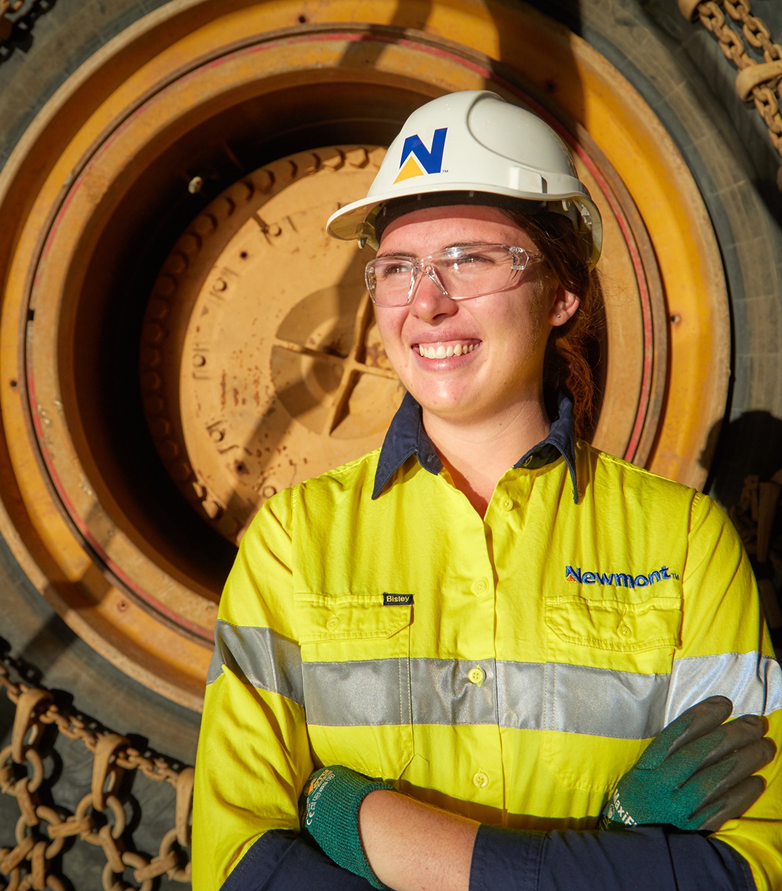 A Newmont worker in a hard hat and safety glasses beside industrial machinery