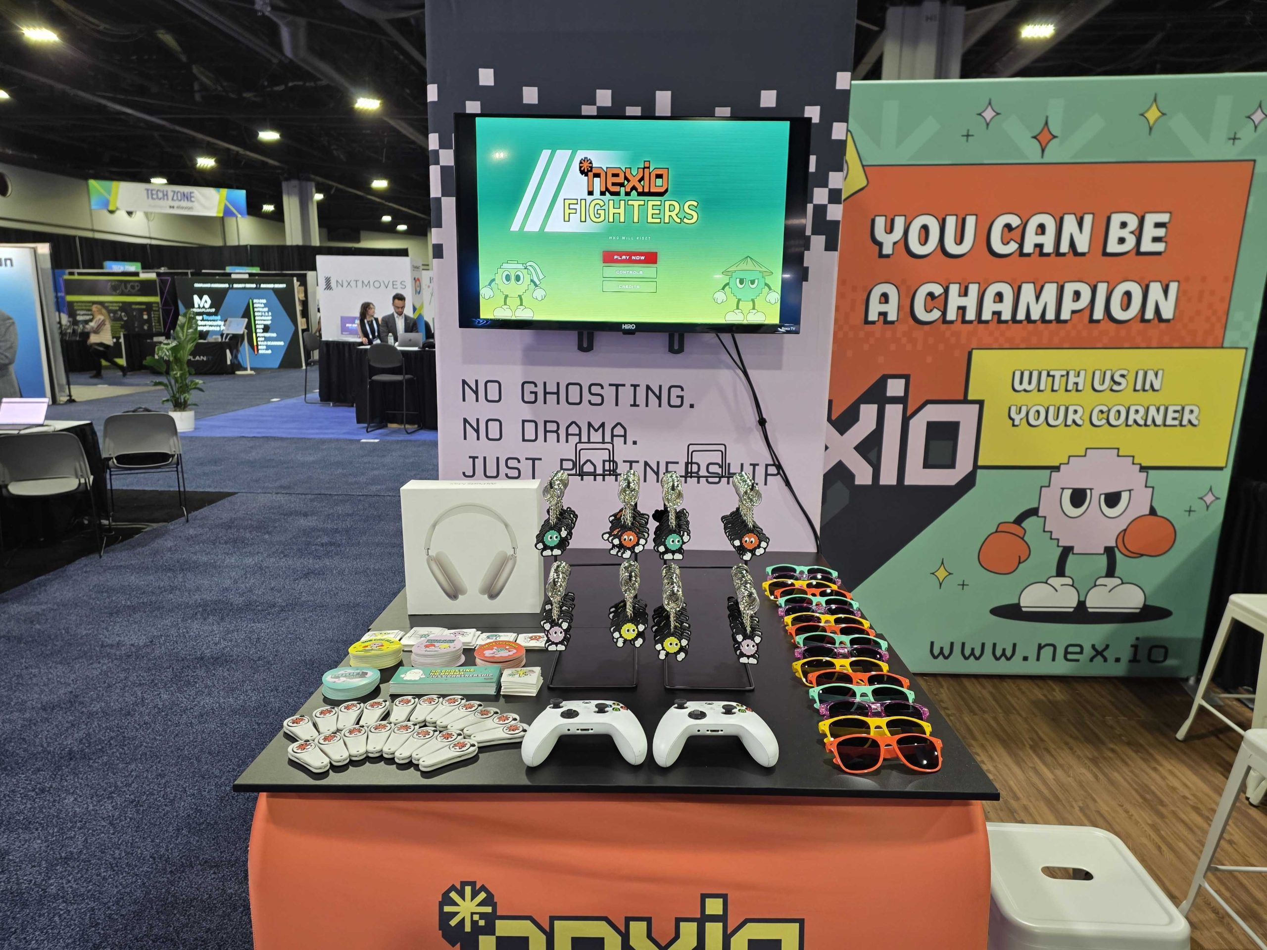 Nexio trade-show booth with a Nexio Fighters game, controllers, keyrings and colorful sunglasses