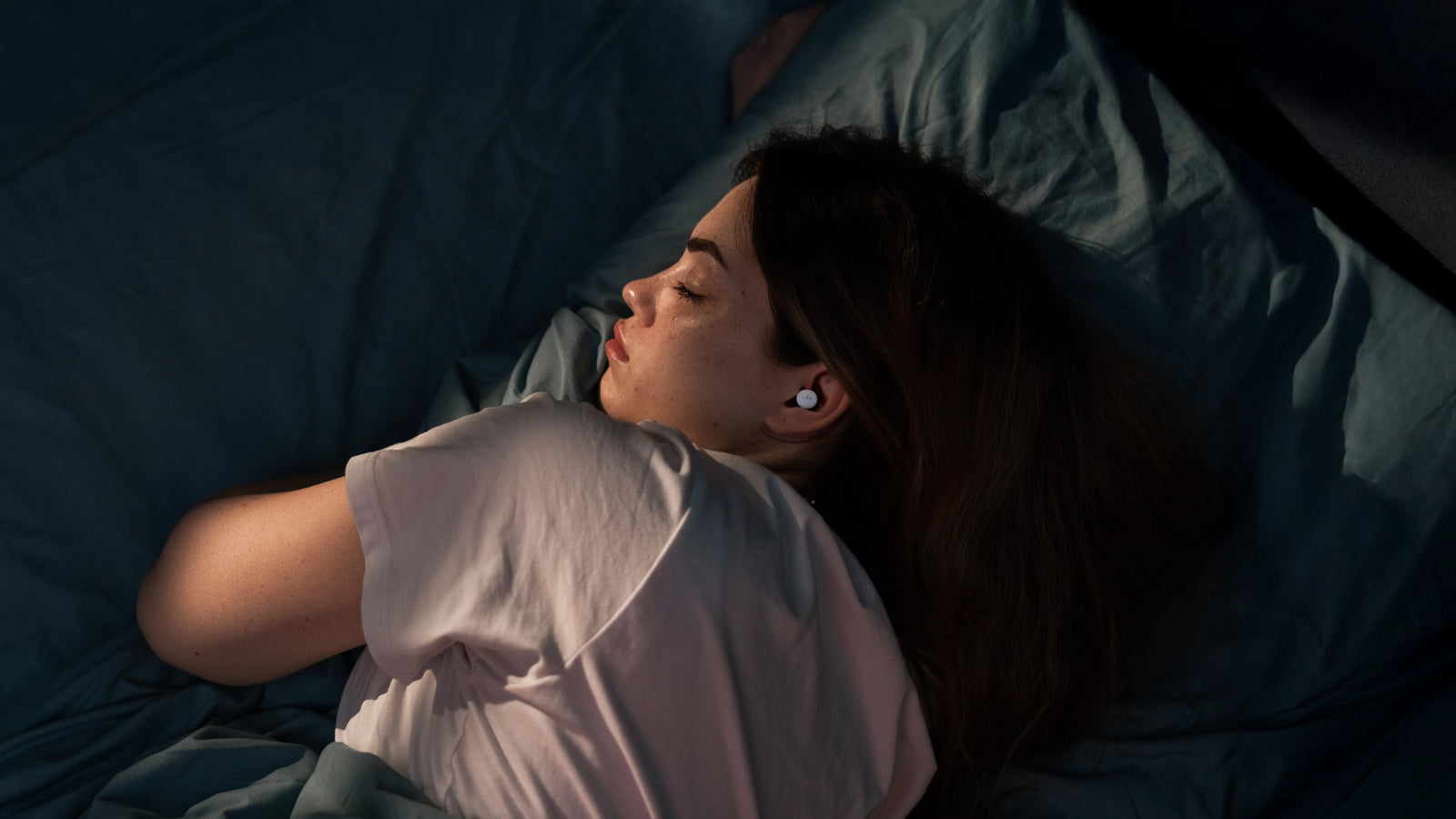 A person sleeping on their side with a NextSense earbud in place