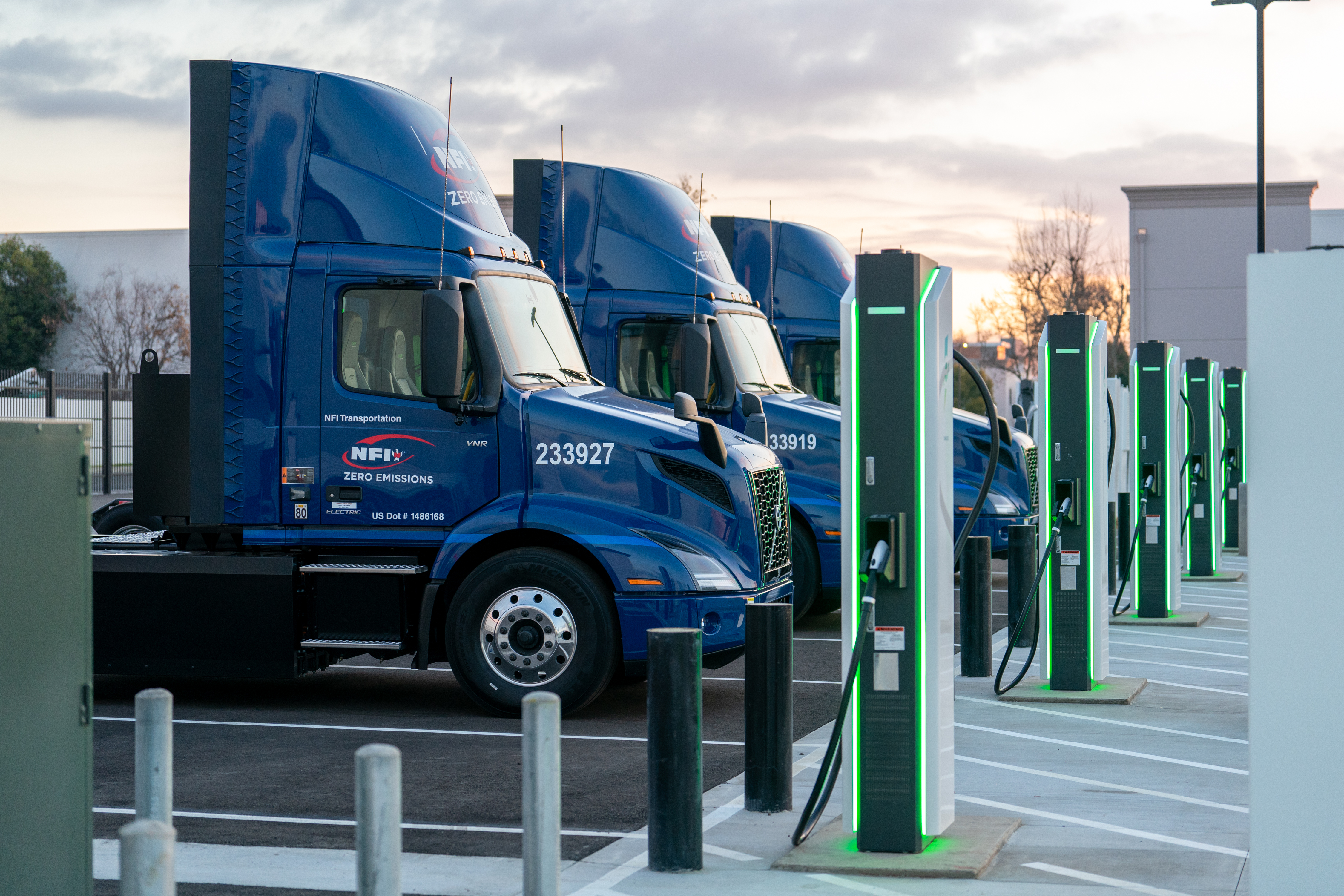 Blue NFI Volvo electric trucks lined up beside charging equipment