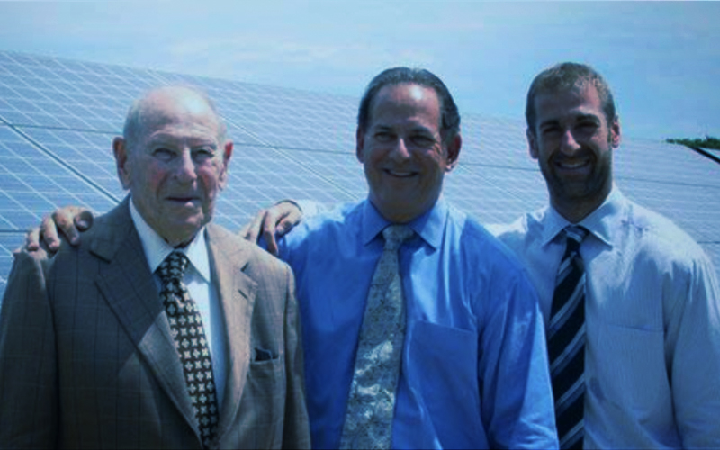 Three Brown family members standing together beside solar panels in an archival company photograph
