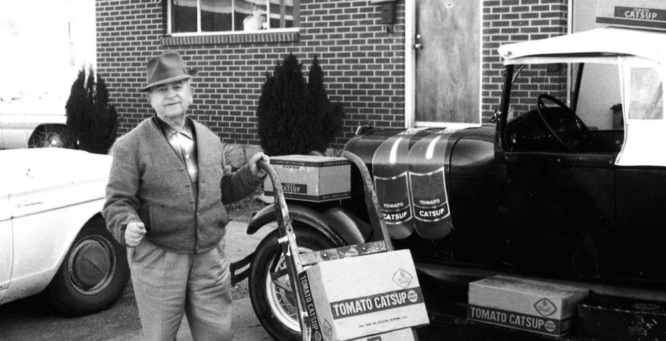 Archival photograph of founder Nicholas Mouskondis carrying boxes for a delivery