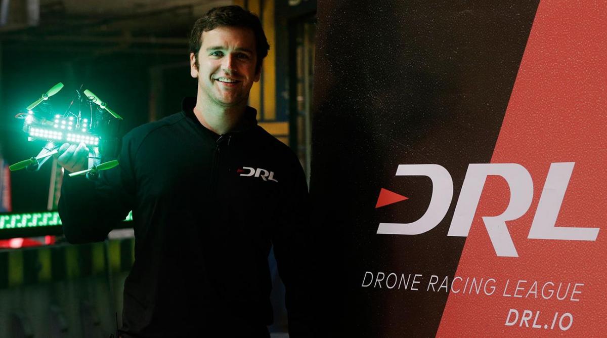 Nicholas Horbaczewski holds a green-lit racing drone beside a DRL banner