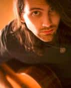 A younger Nick Ganju holding a guitar in a warmly lit photograph