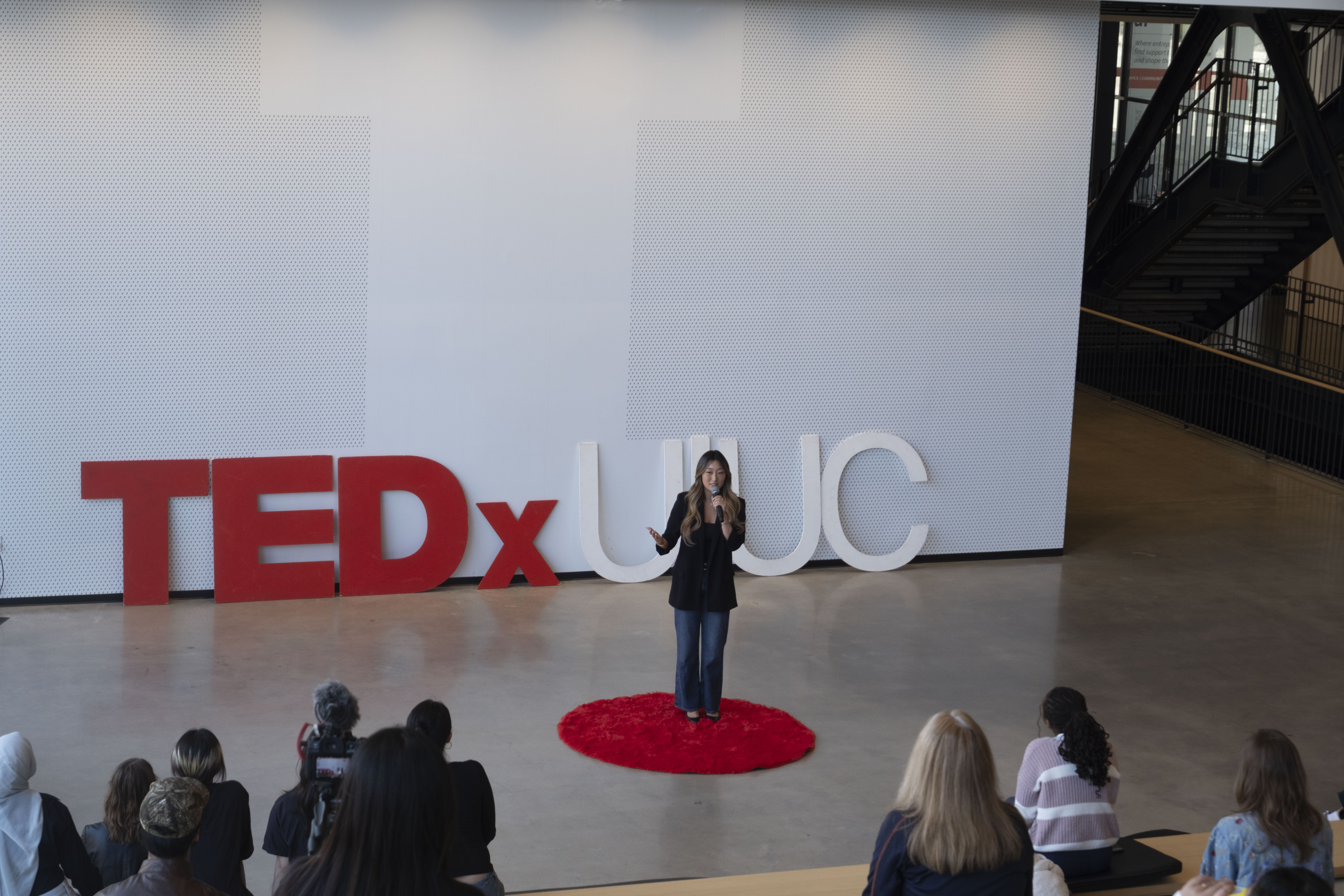 Paige Taylor speaking on the red TEDxUIUC carpet before a seated audience