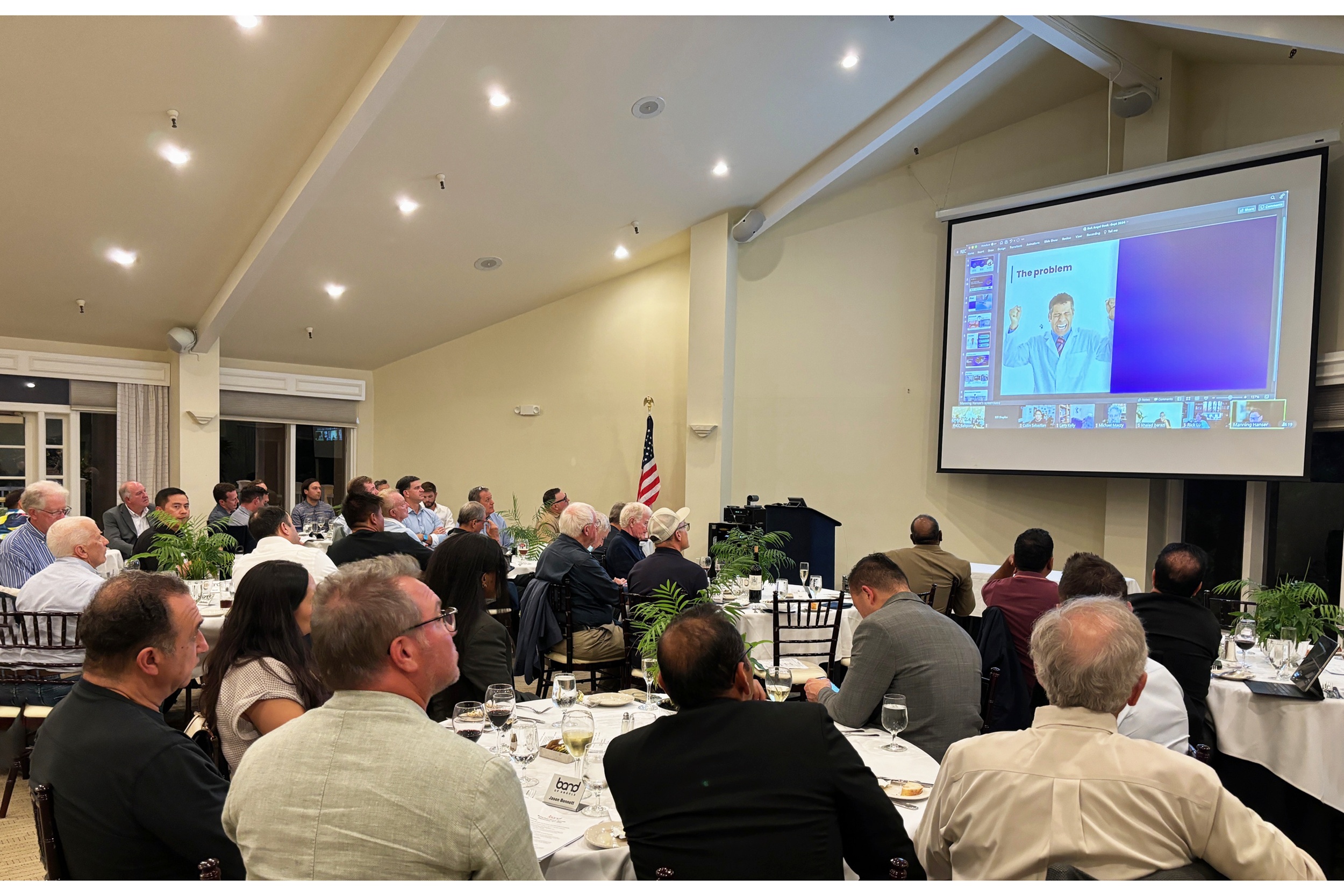 Attendees seated at tables watch a startup presentation at a Band of Angels deal dinner.