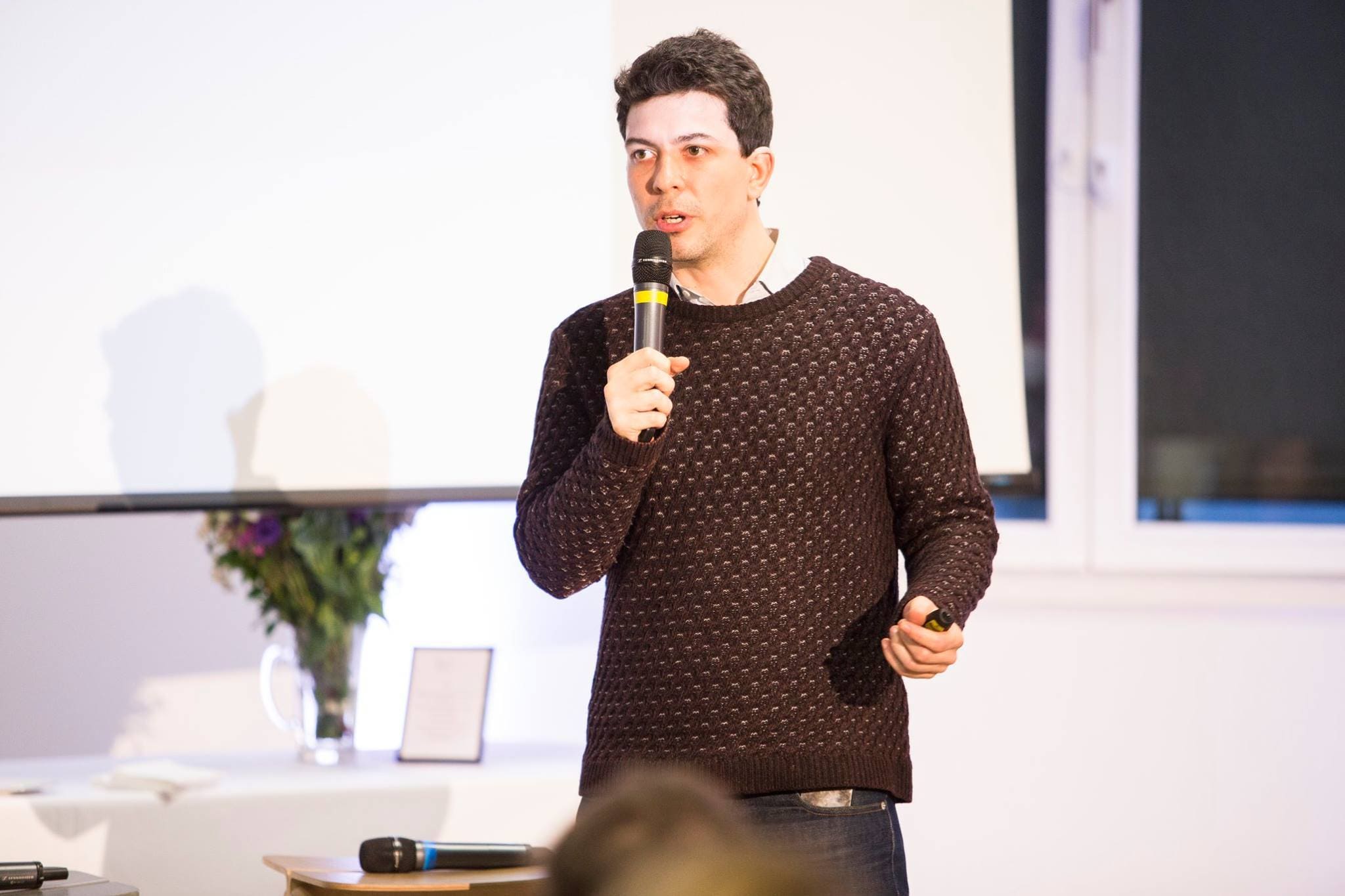 Nicolas Hernandez speaking into a handheld microphone in front of a projection screen
