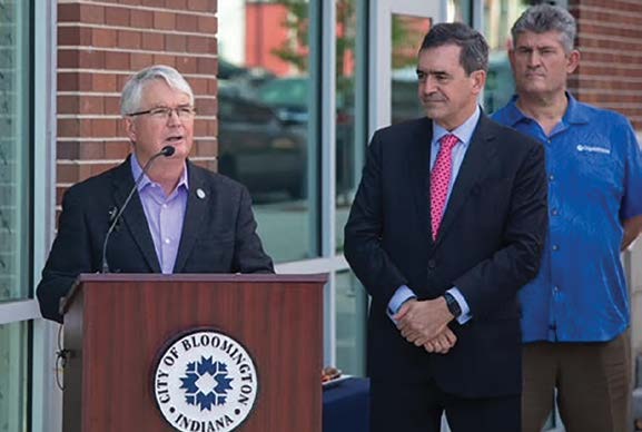 Bloomington Mayor John Hamilton speaks at a podium while Nicolas Rubio stands beside him, wearing a red tie.