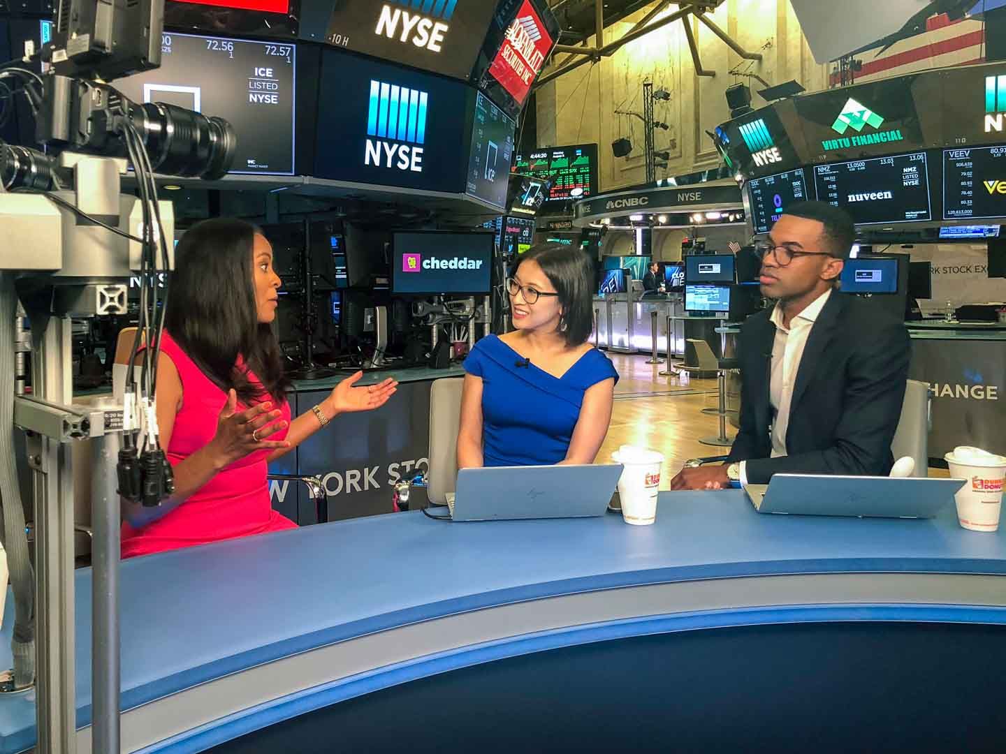 Nicole Gibbons, at left in pink, speaking with two television presenters on the New York Stock Exchange floor