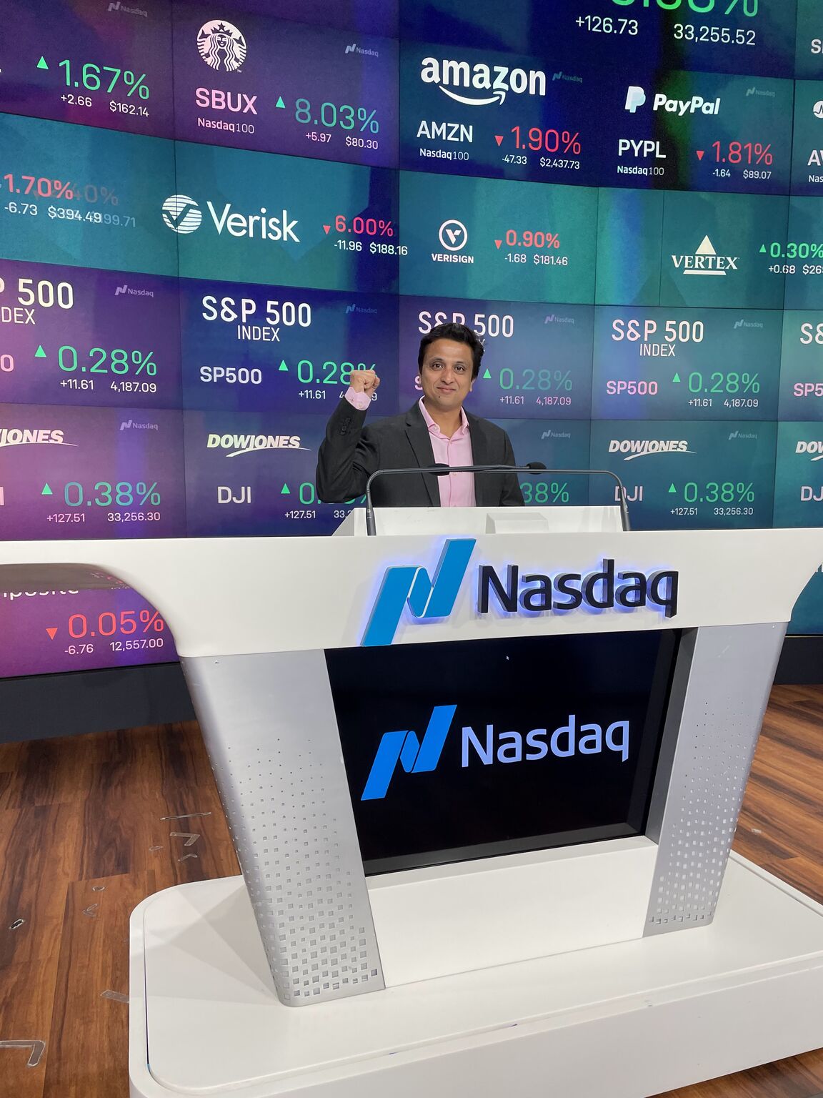 Nikhil Gupta at a Nasdaq podium with market displays behind him