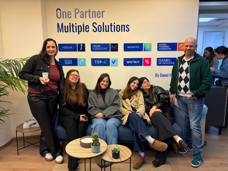 Six colleagues gathered on and beside a sofa beneath signs for Nisha and other Danel HR businesses