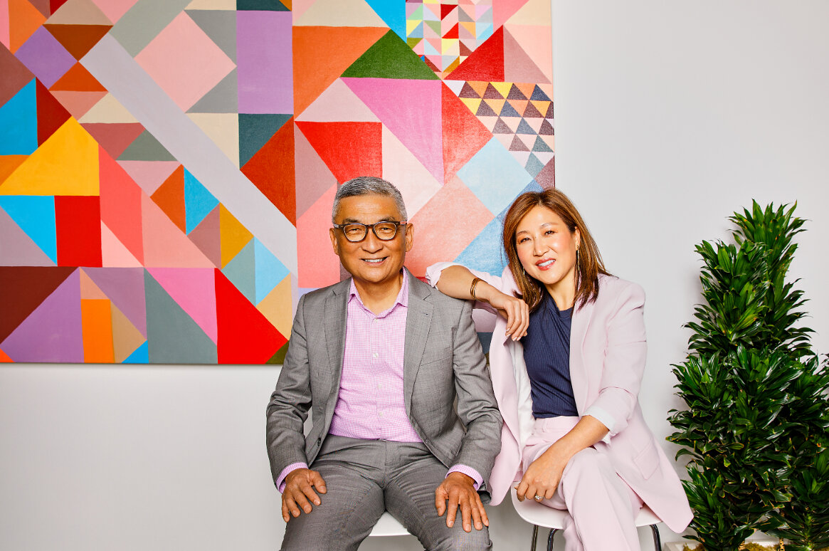 Bill Imada and Nita Song seated together in front of a colorful geometric wall