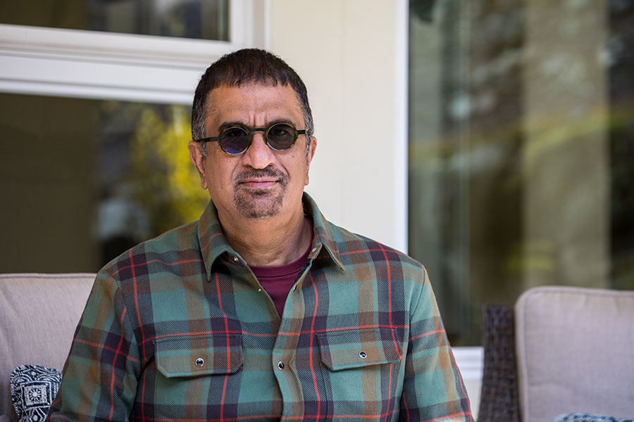 Nitin Rai seated outdoors, wearing a green plaid shirt and round glasses