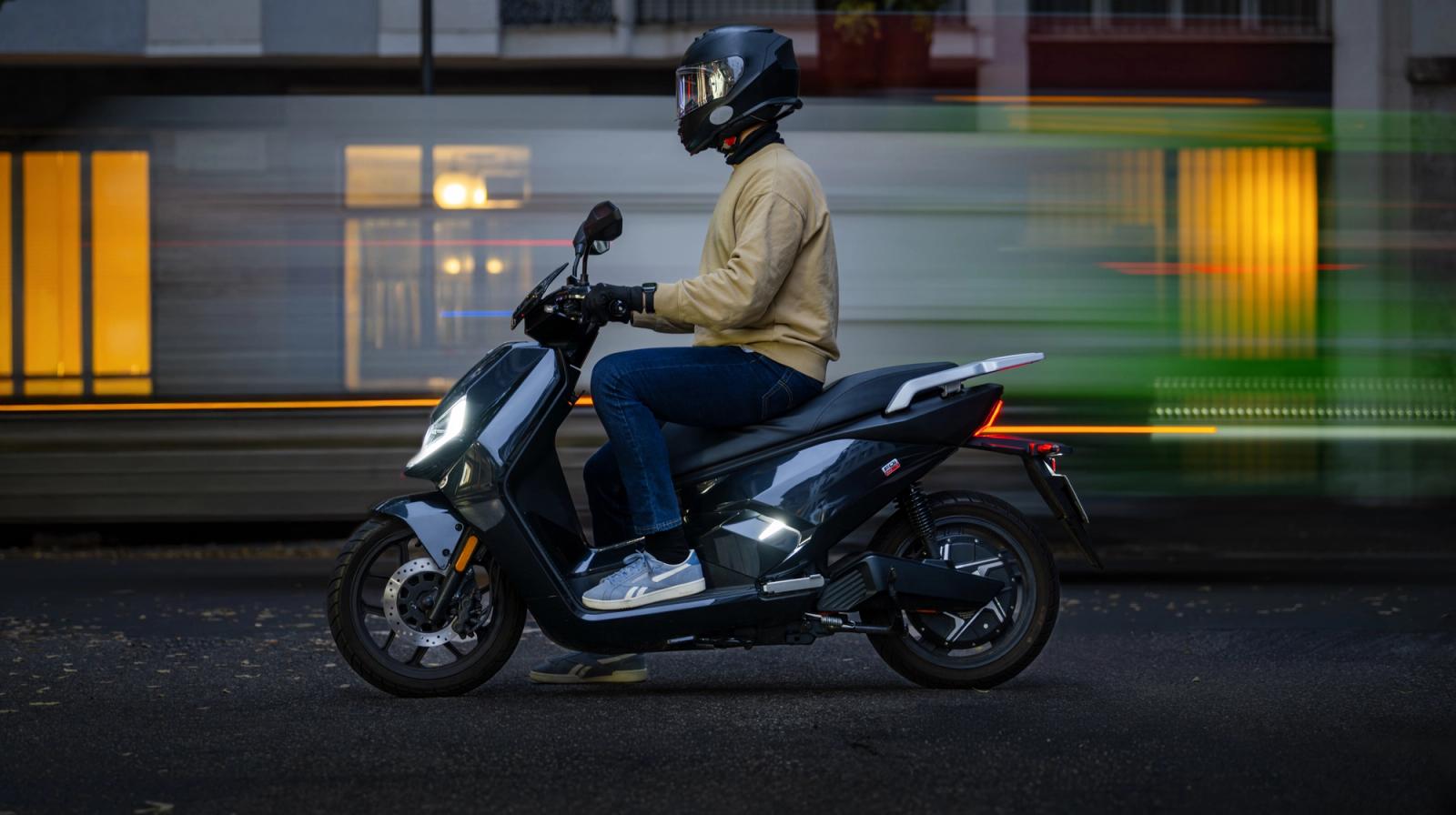 Helmeted rider on a NIU seated electric scooter beside city buildings