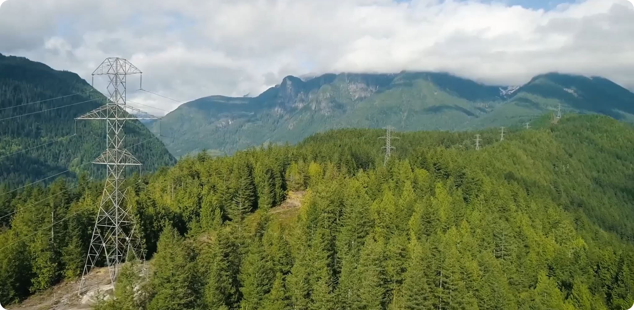High-voltage transmission towers crossing a forested mountain landscape