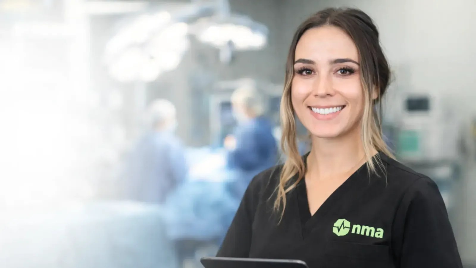 NMA neuromonitoring clinician in scrubs beside a tablet in an operating room