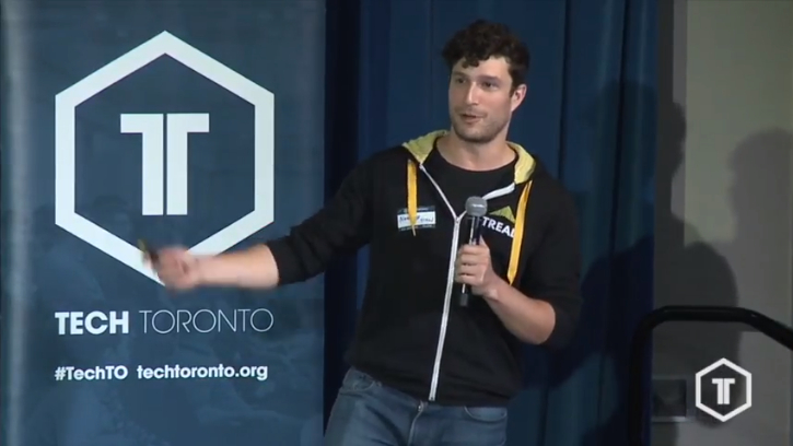 Noah Dolgoy speaking into a handheld microphone at TechTO