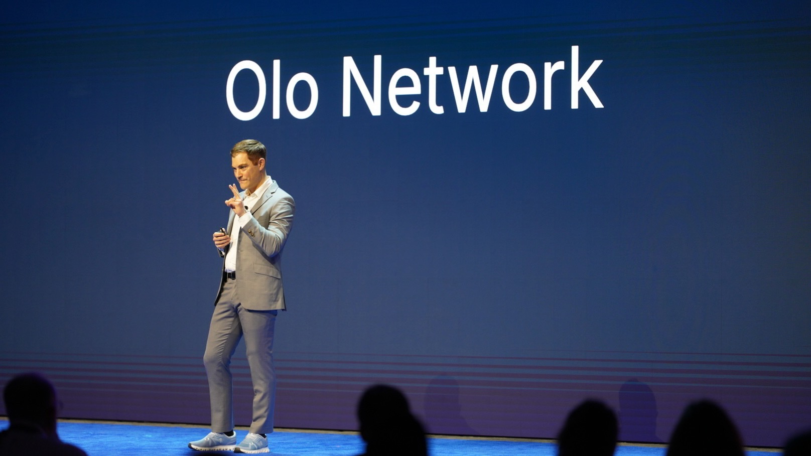 Noah Glass presents Olo Network on stage in a gray suit and sneakers.