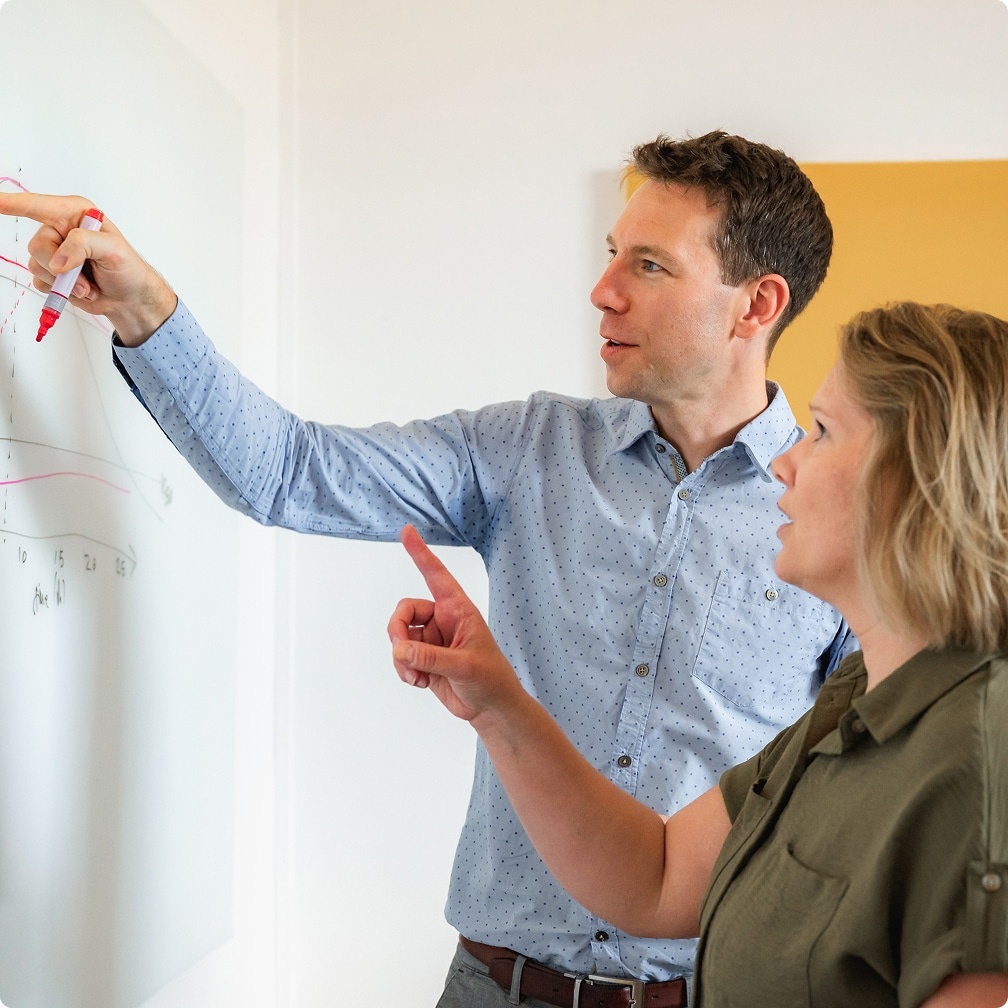 Two people discussing diagrams at a whiteboard in a company photograph