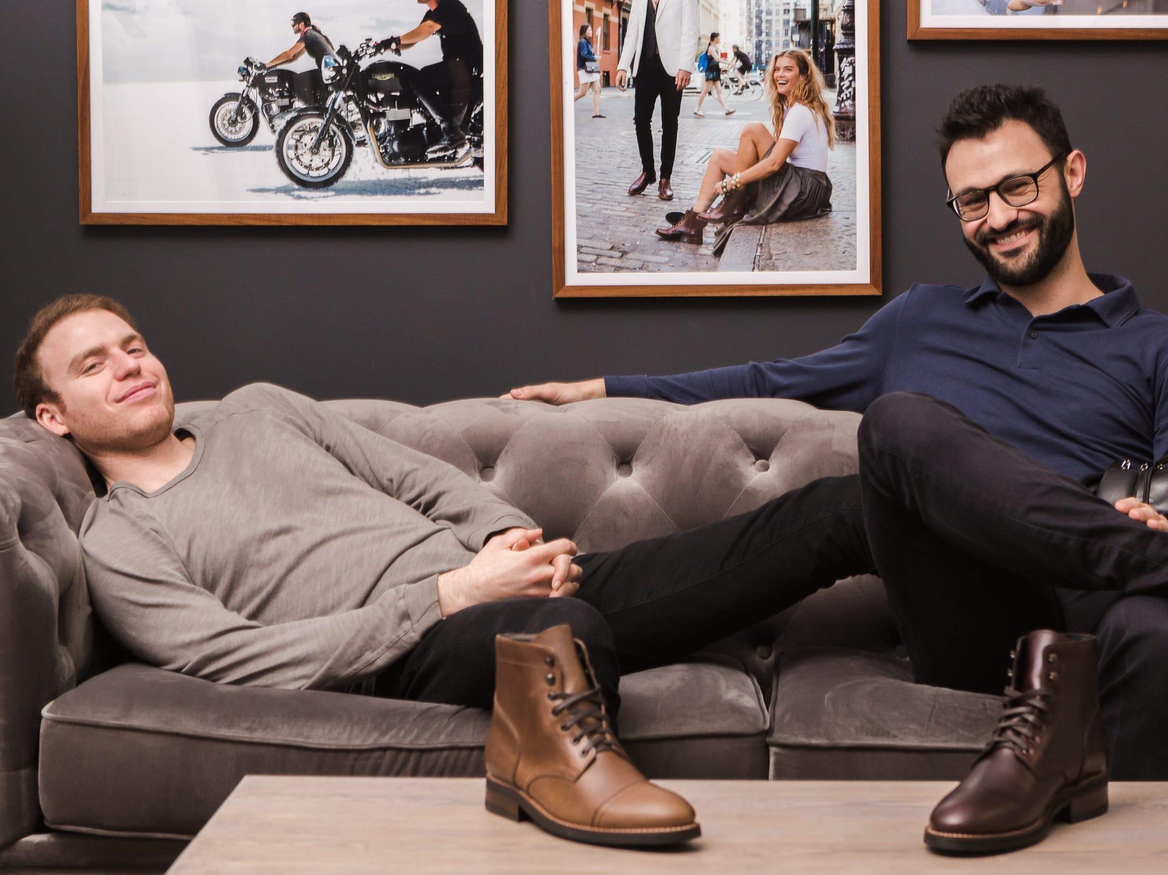 Nolan Walsh on the left and Connor Wilson on the right, seated on a showroom sofa with boots on the table