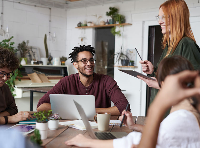 People collaborating around laptops in an illustrative image published on Noosh's About page