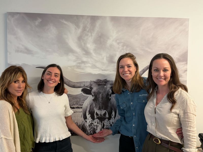 Four colleagues gather in an office in front of a large photograph of a Texas longhorn