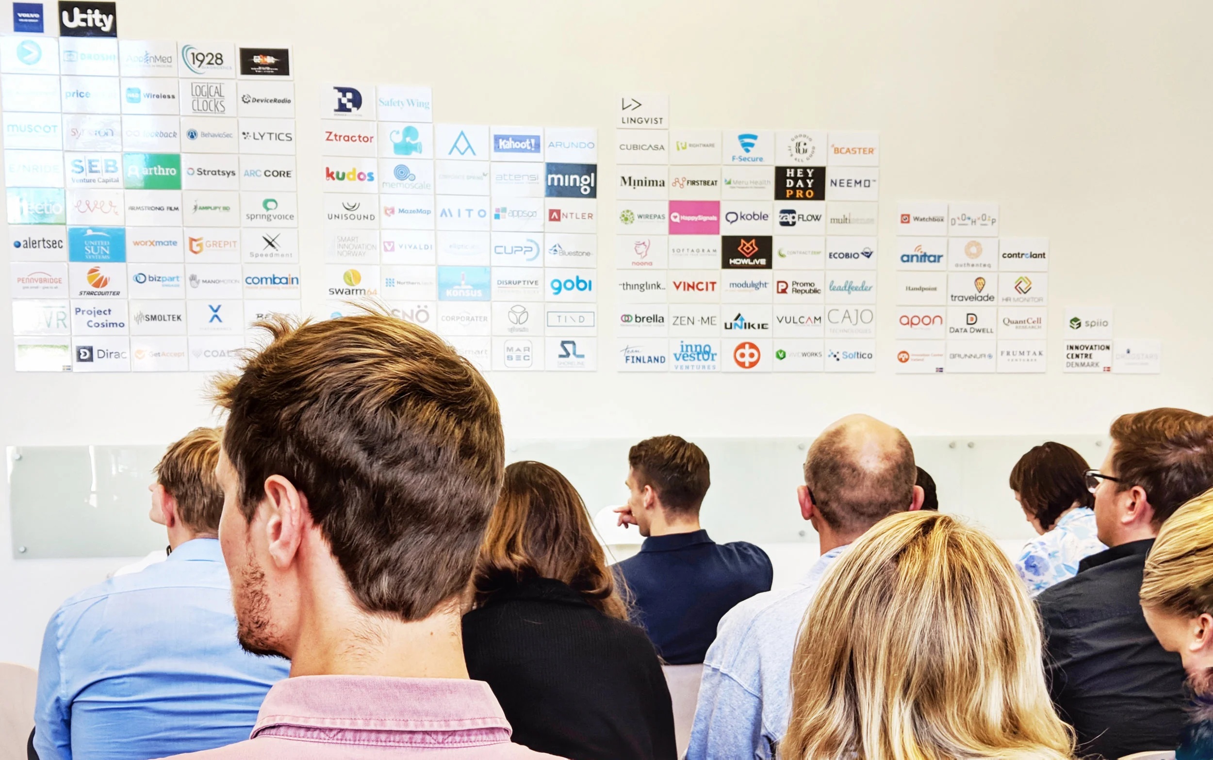 People seated beneath a wall of company logos at Nordic Innovation House