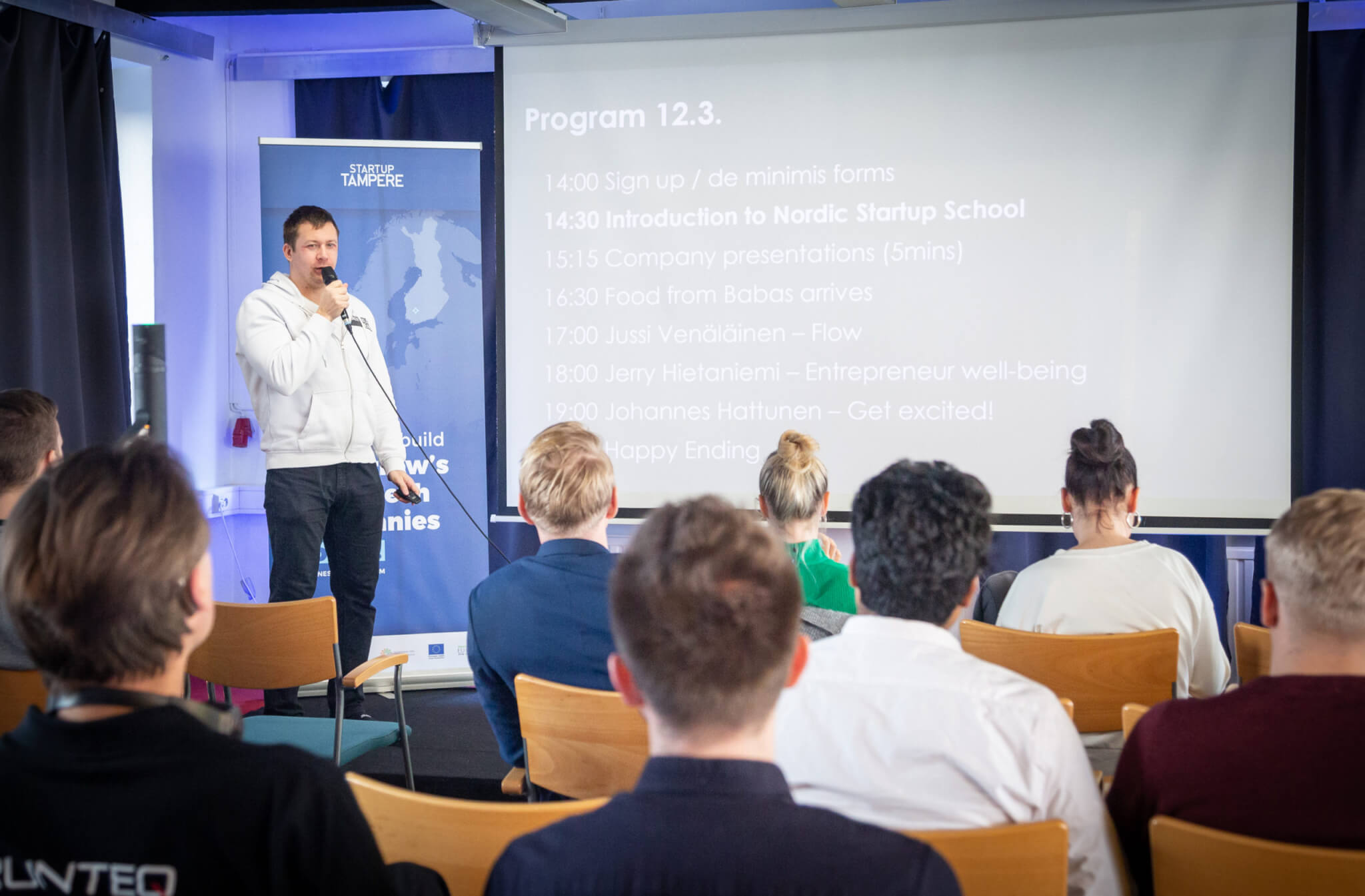 Nordic Startup School participants seated at a workshop with a speaker and projected schedule