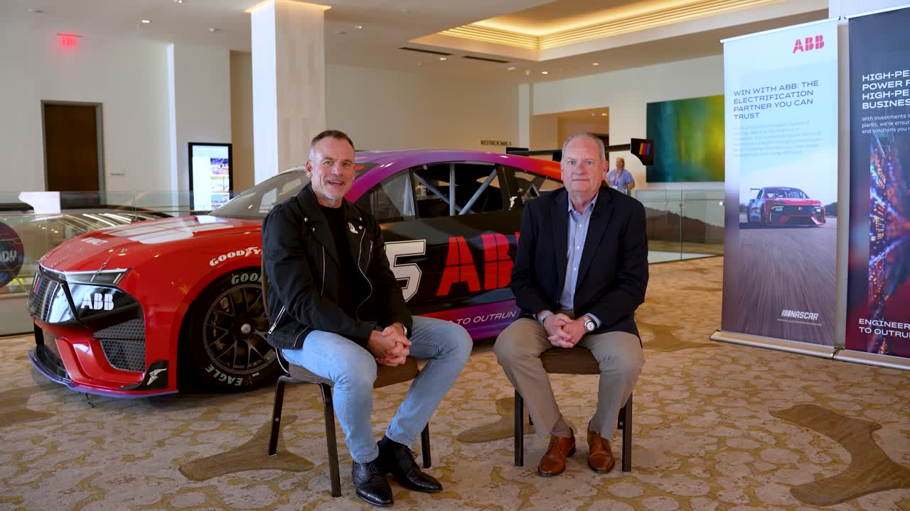 Norm Sowards and Trade Hounds CEO David Bauders seated in front of an ABB-branded electric NASCAR prototype