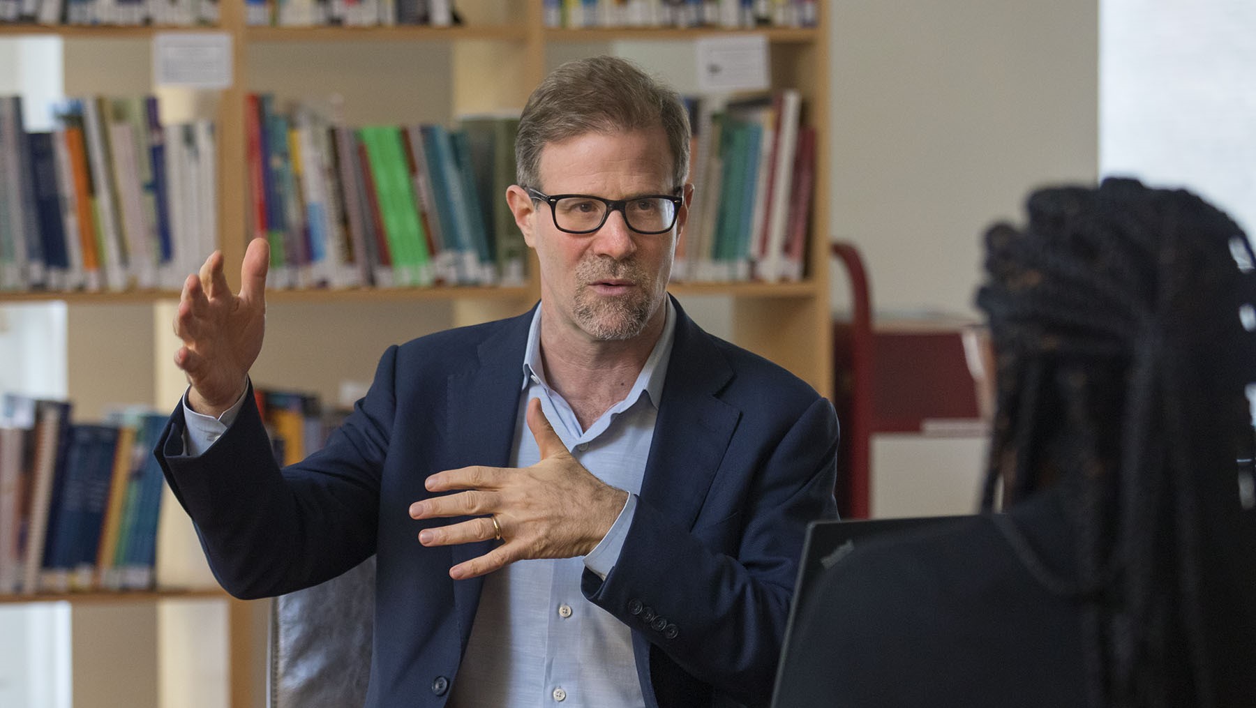 Norman Atkins gesturing during a conversation in a room lined with books