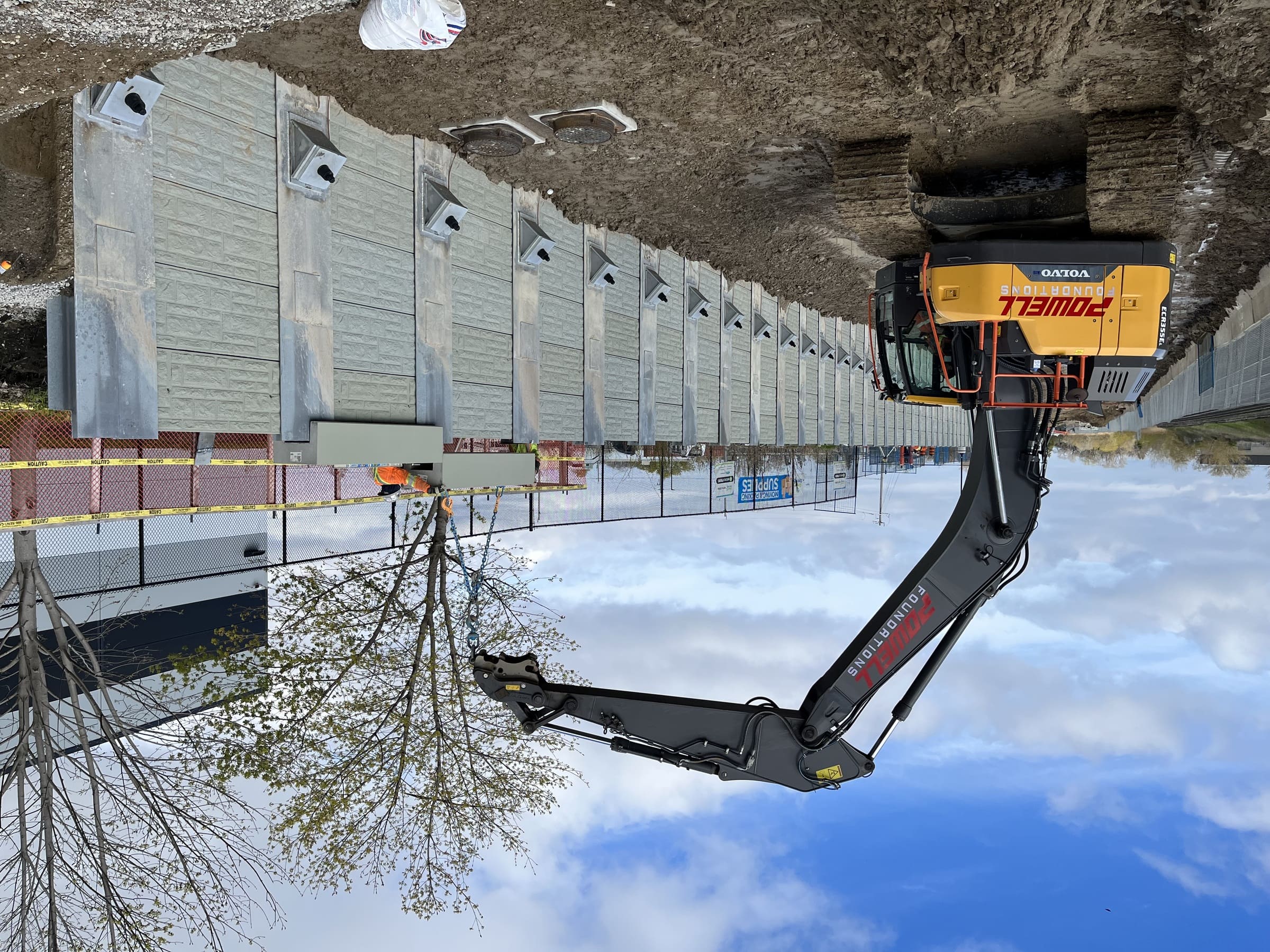 Powell Foundations excavator and workers lifting a wall panel into position beside a rail corridor