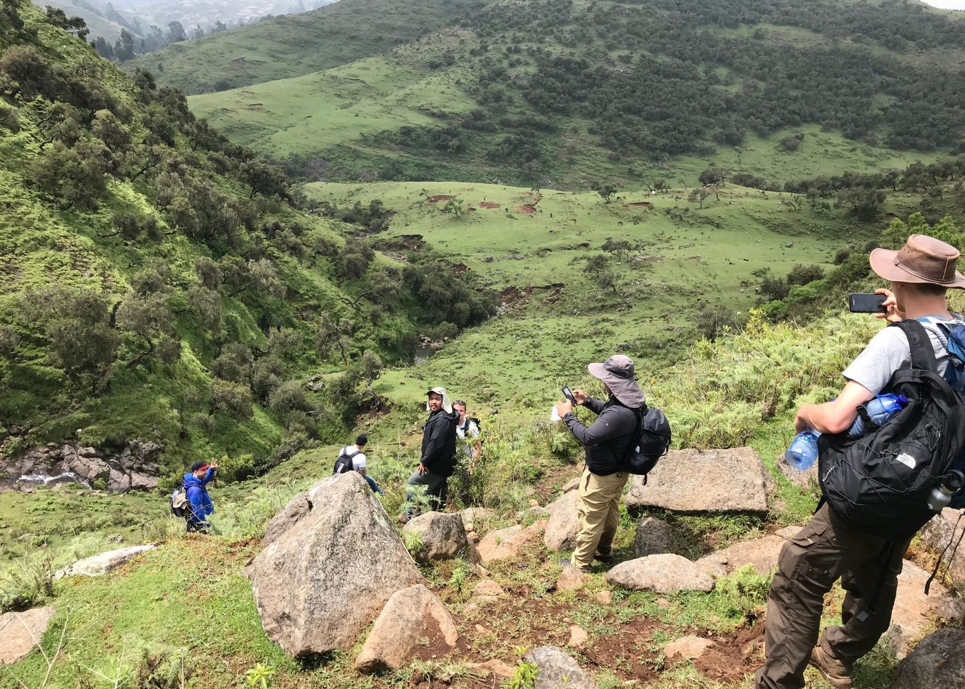 Northland Challenge participants pause on a rocky path above a green mountain valley