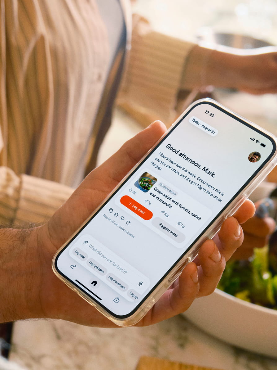 A hand holding a phone displaying the Nourish app with meal logging and health tracking