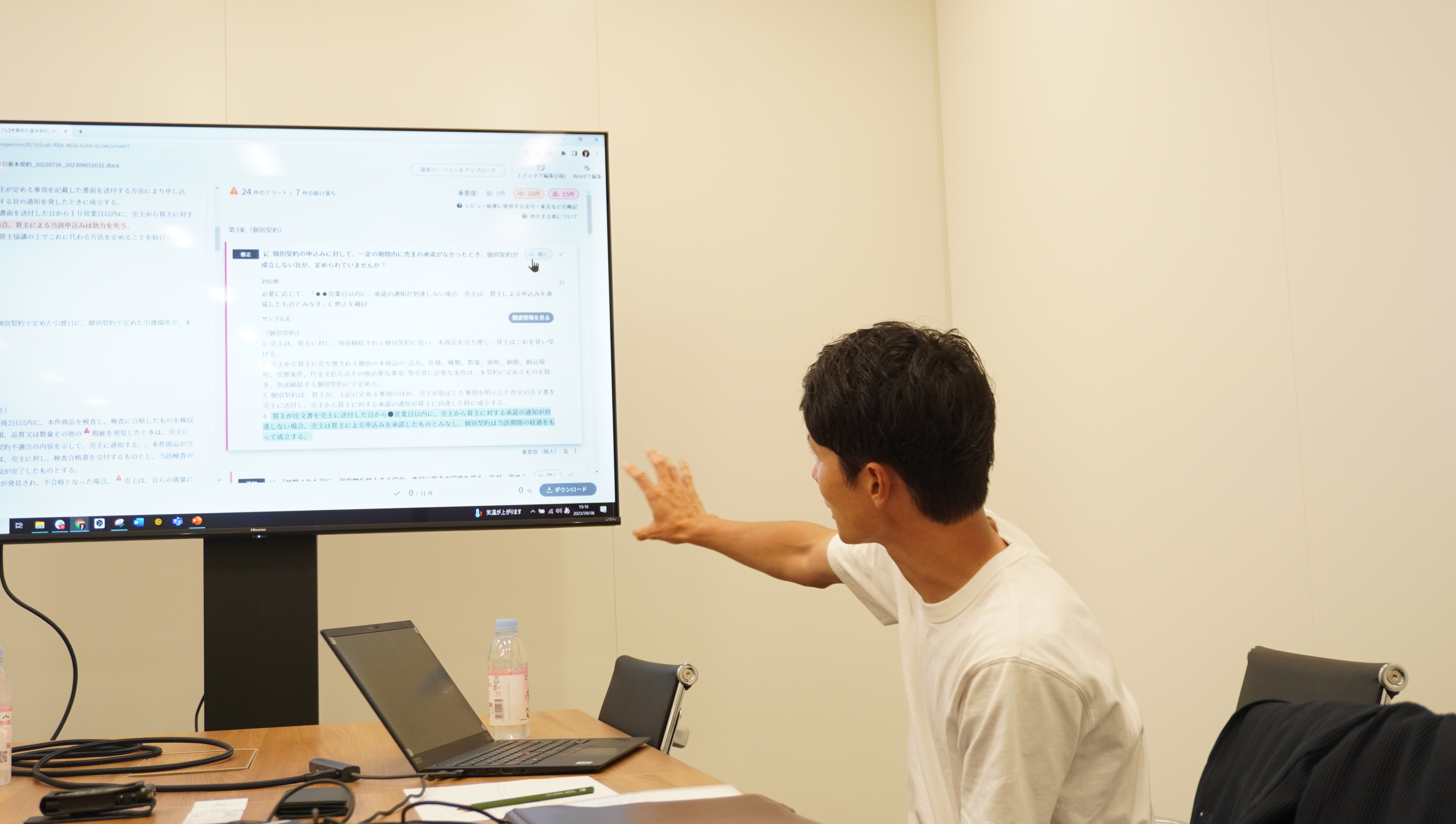 Nozomu Tsunoda in a white T-shirt demonstrating LegalForce on a meeting-room screen