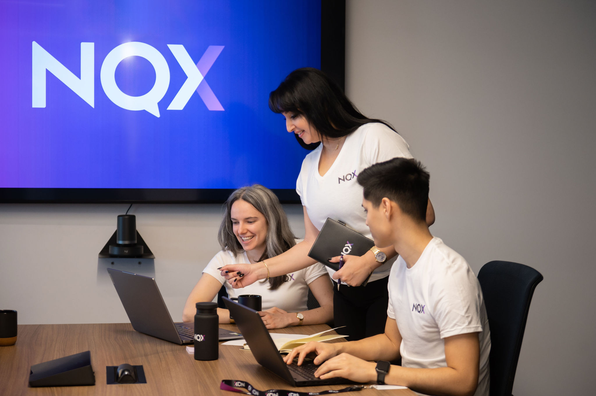 Three NQX colleagues collaborating around laptops in a meeting room