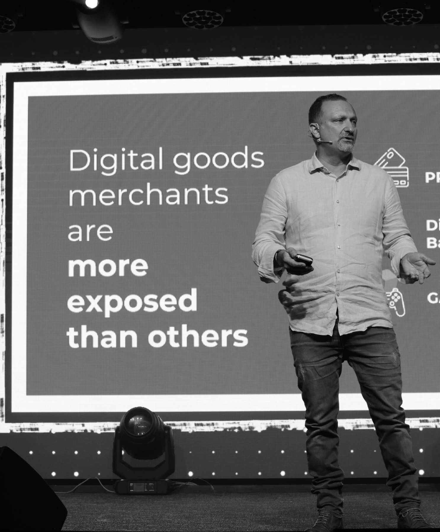 Alex Zeltcer presenting on a stage beside a slide about digital merchants’ exposure to fraud