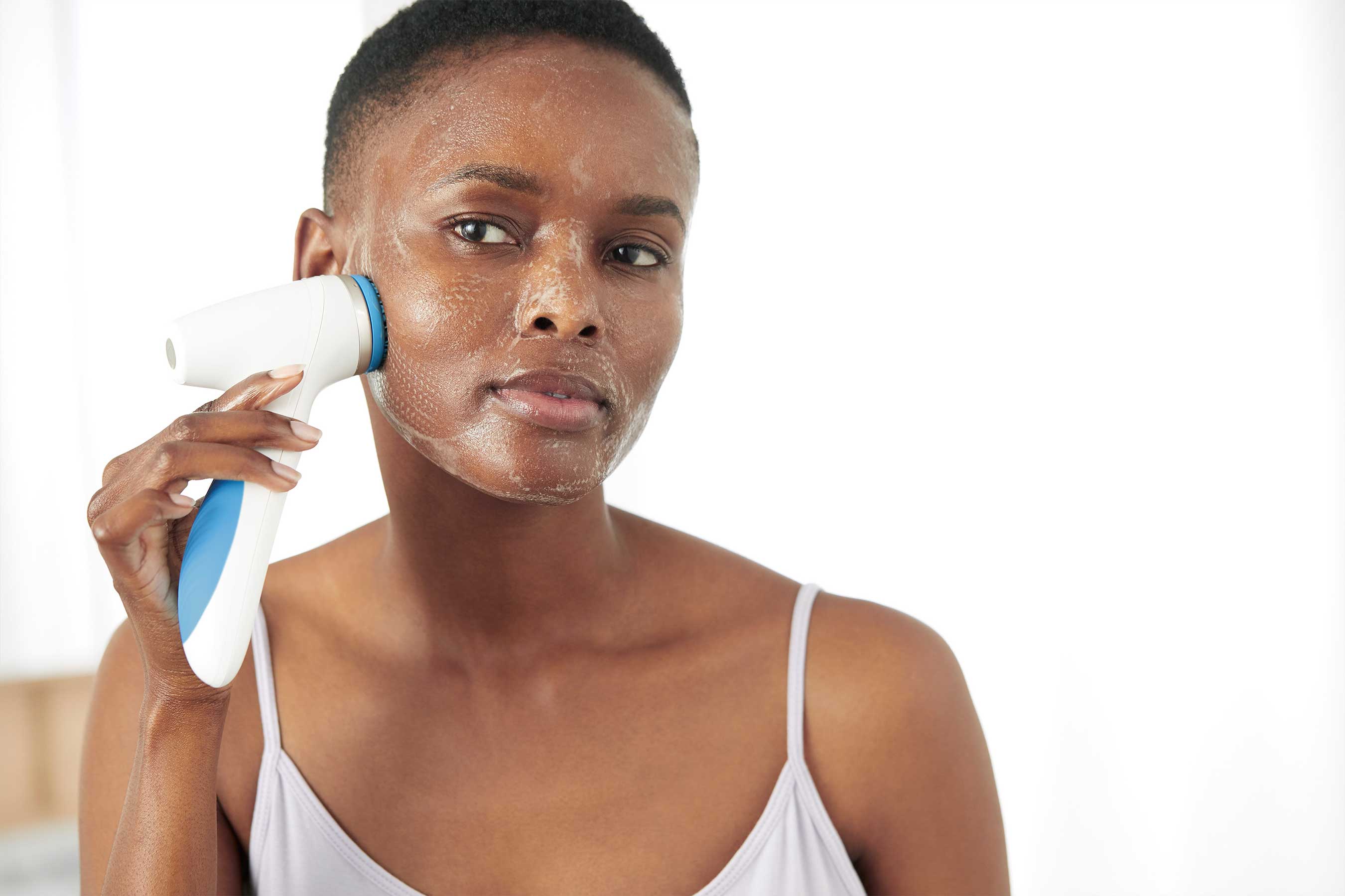 A woman demonstrating the LumiSpa iO cleansing device against her cheek