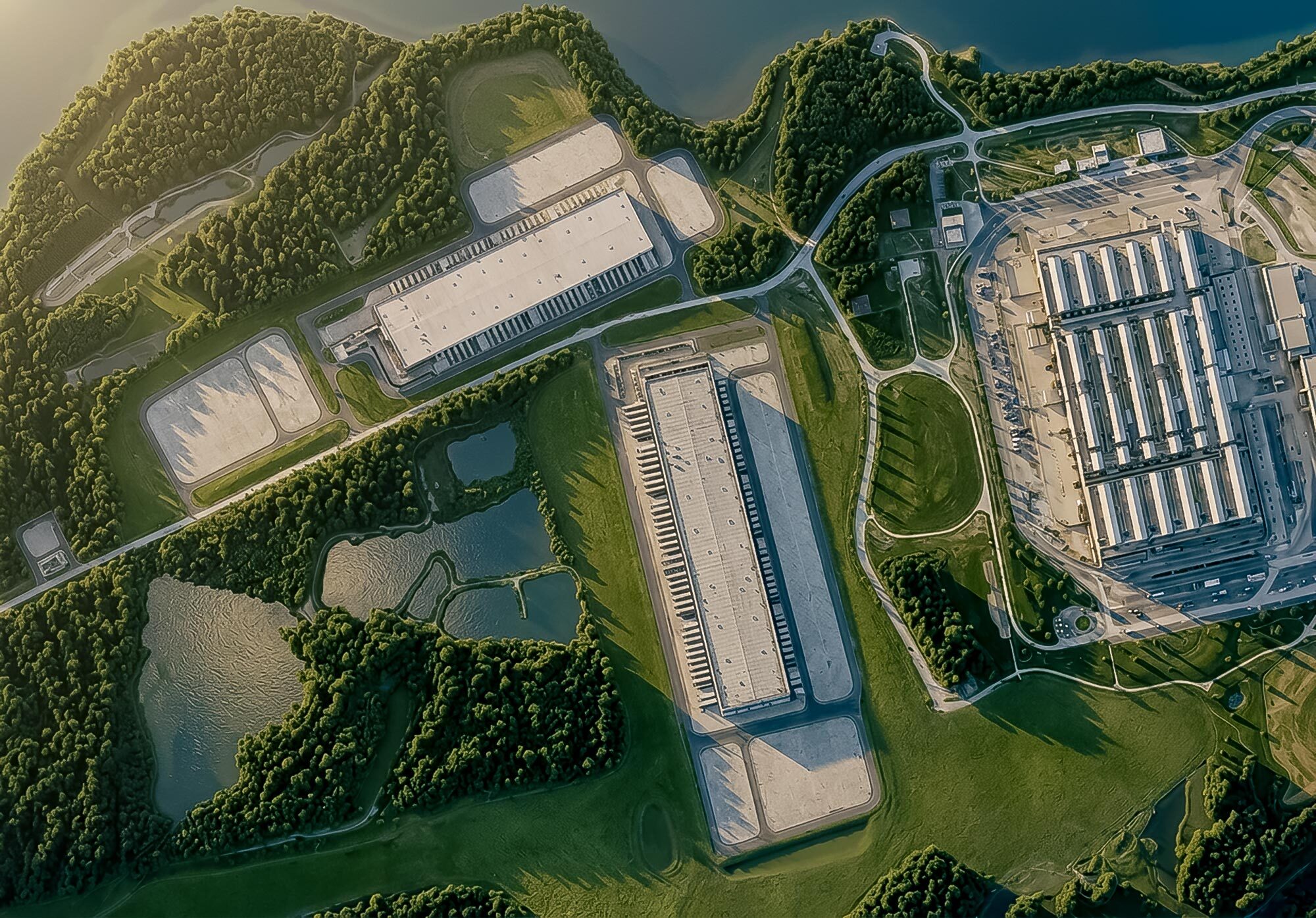 Aerial campus image showing large industrial buildings, access roads, trees, and water